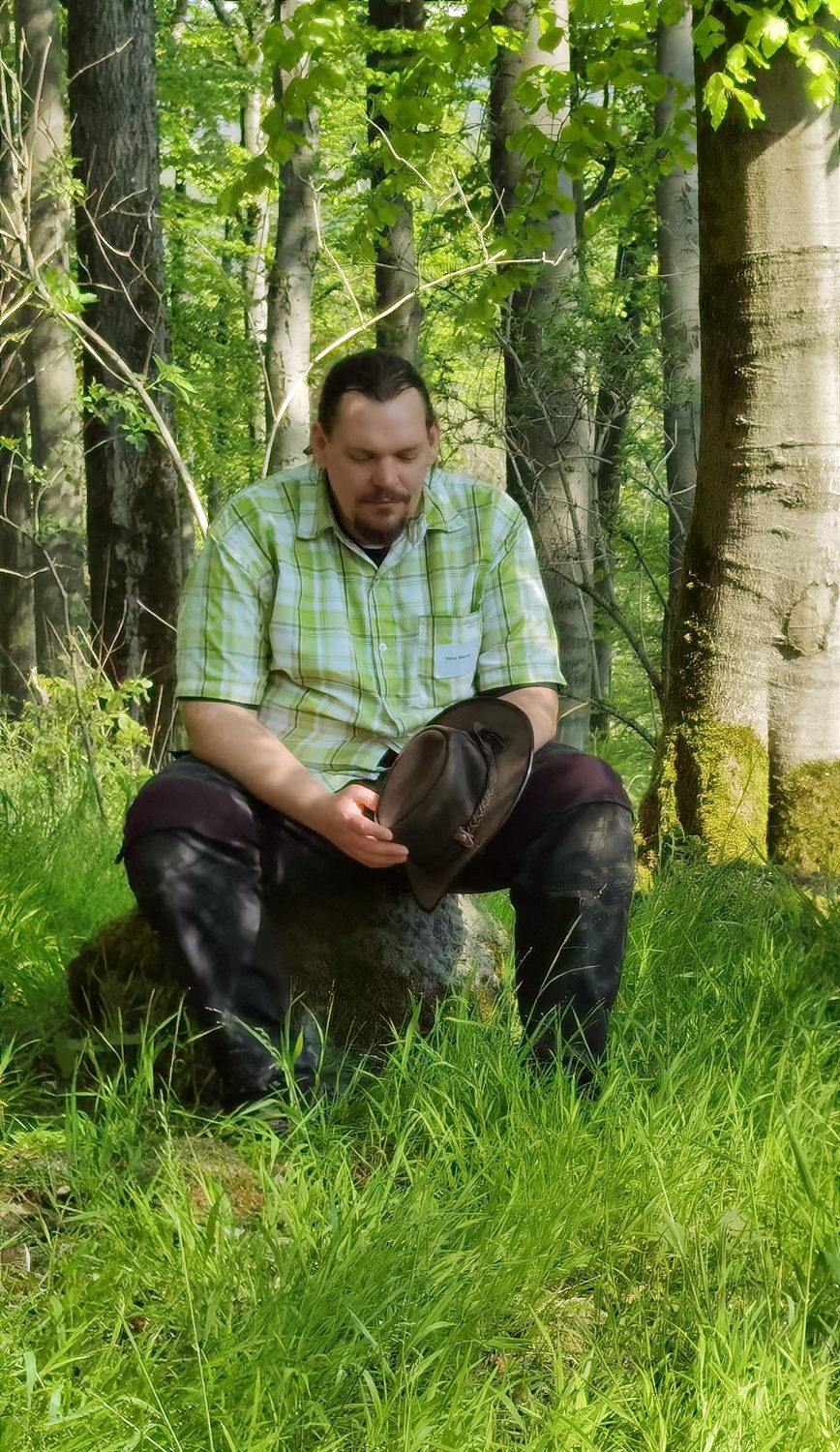 Peter sitzt nachdenklich im Wald, den Hut in der Hand